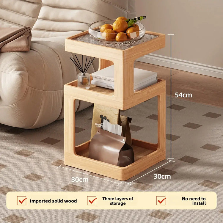 Wooden side table with storage compartments, placed on a patterned carpet next to a beige sofa.