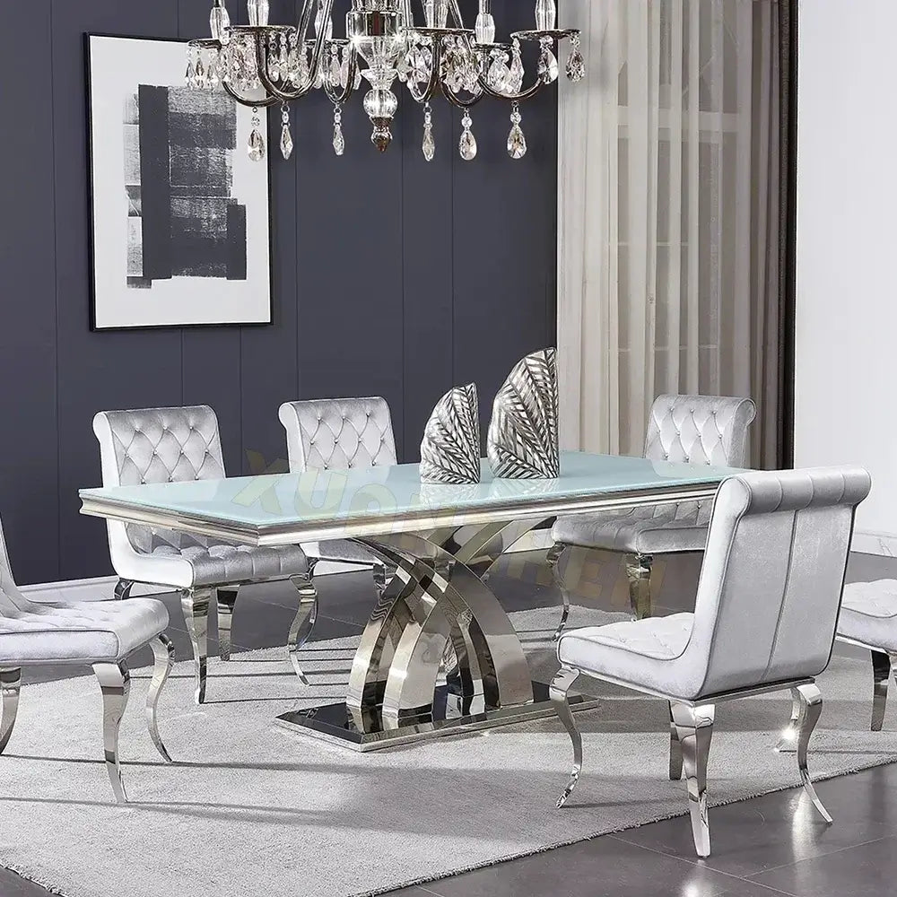 Modern dining room with a glass table and silver chairs against a gray wall.