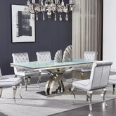 Modern dining room with a glass table and silver chairs against a gray wall.