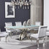 Modern dining room with a glass table and silver chairs against a gray wall.