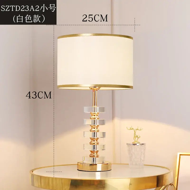 Modern crystal table lamp with fabric shade on a side table, featuring a gold finish and clear crystal body.