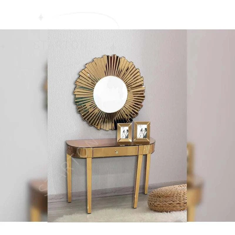 Gold console table with round mirror and framed photos against a light gray wall.
