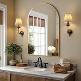 Arched metal framed bathroom mirror in modern bathroom setting with elegant decor and natural lighting.