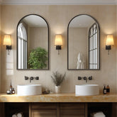 Bathroom vanity with two large arch-shaped mirrors, wall lights, and decorative items.