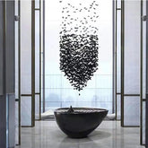 Black butterfly sculpture above a black bowl in a modern indoor setting with large windows.