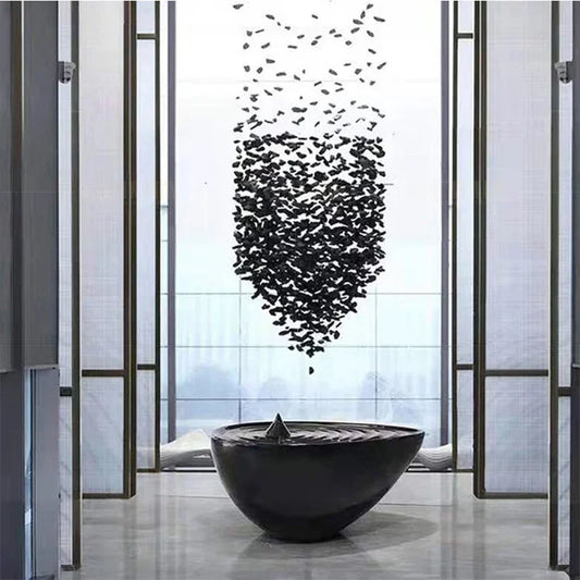 Black butterfly sculpture above a black bowl in a modern indoor setting with large windows.
