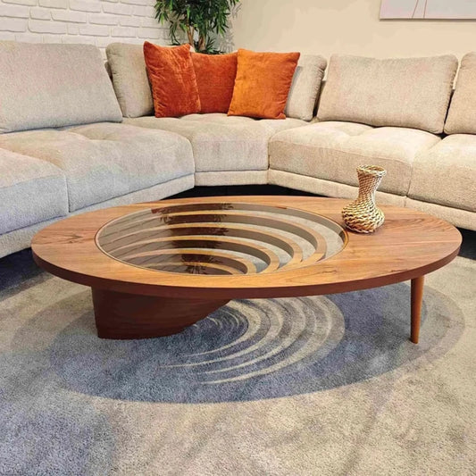 Round wooden coffee table with glass top in front of a sectional sofa with orange cushions.