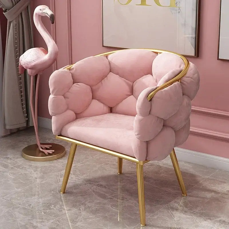 Pink armchair with gold legs in a room with a pink wall and a flamingo decoration.