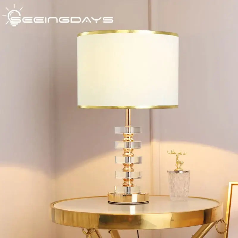 Modern crystal table lamp with fabric shade featuring gold accents and a clear crystal body.