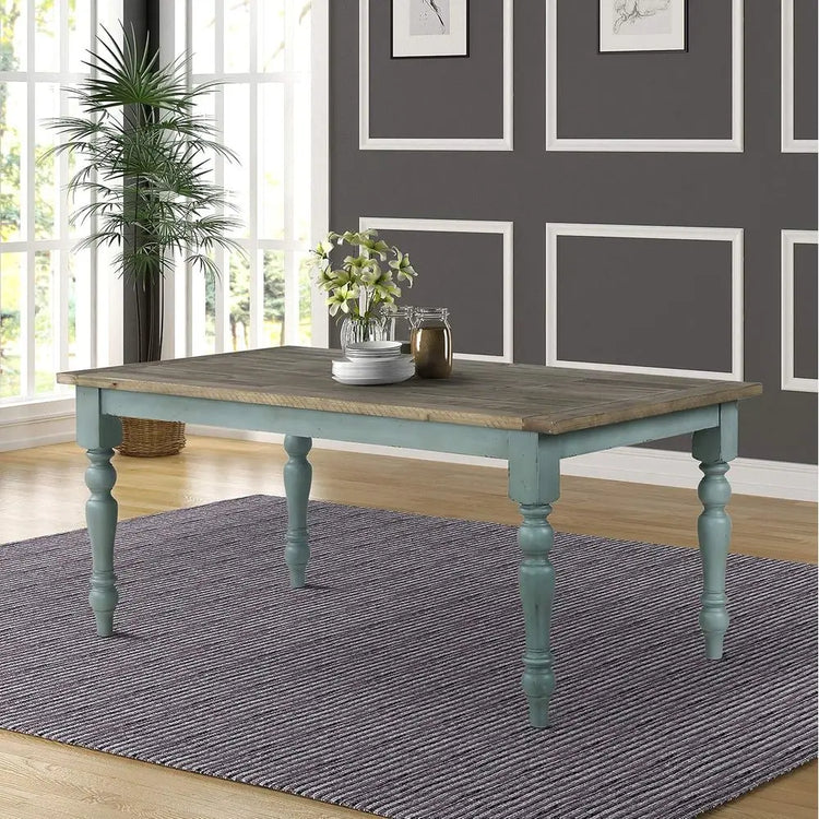 Wooden dining table with teal legs in a room with gray walls and large windows.