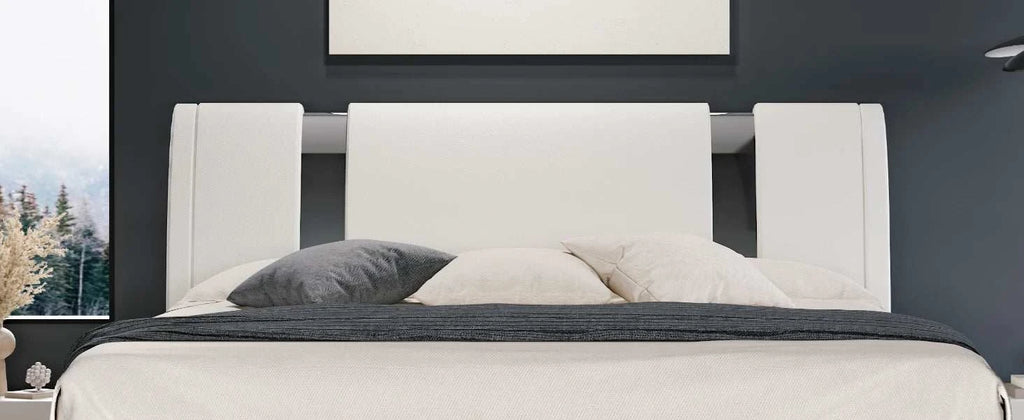White upholstered bed with gray bedding against a dark wall