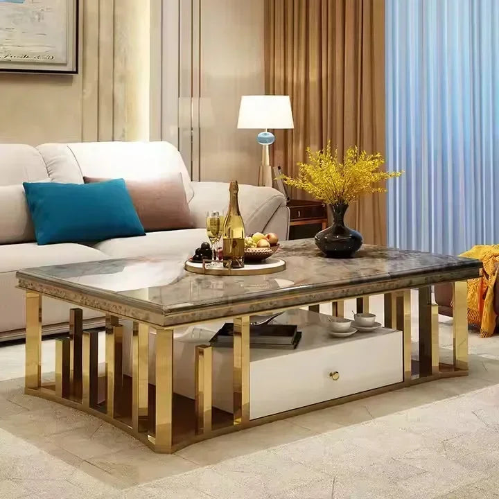 A modern rectangular coffee table with a dark gray marble-patterned top and gold-finished metal legs, shown in a styled living room setting with a sofa, lamp, and decorative items.