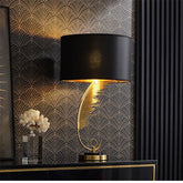Decorative lamp with black shade and gold base against a patterned wall.