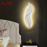 Decorative wall lamp shaped like a feather in a bedroom setting with ULANI branding.