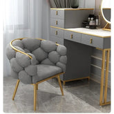 Gray upholstered chair with gold accents in a room with a vanity table.