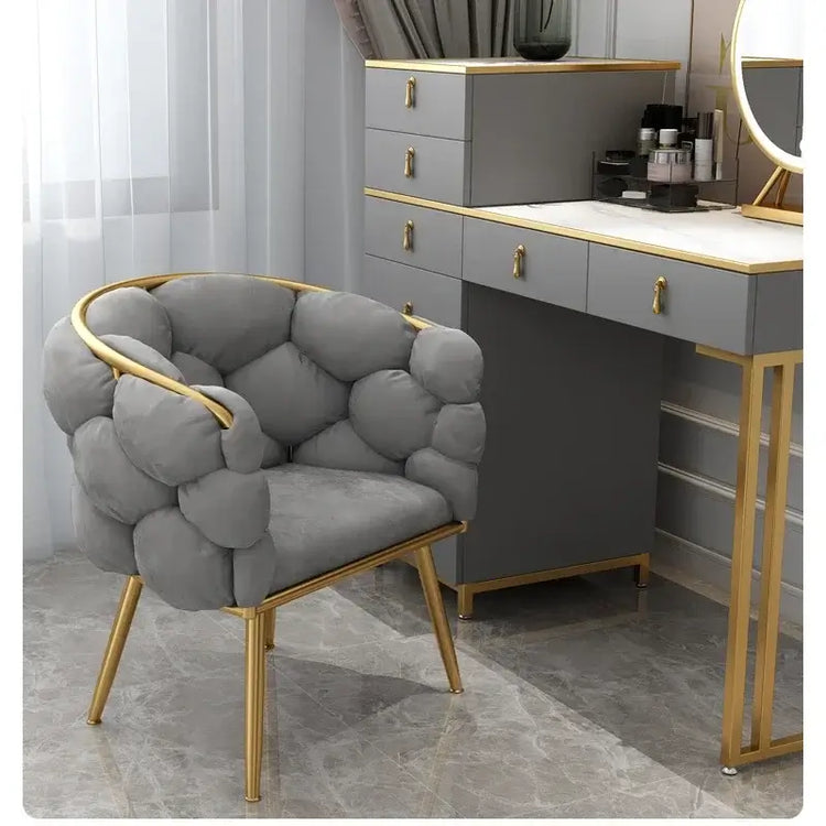Gray upholstered chair with gold accents in a room with a vanity table.