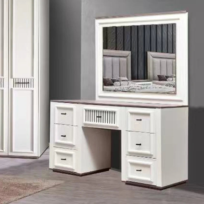 White vanity desk with an attached rectangular mirror, shown in a bedroom setting next to a matching wardrobe. The desk features multiple drawers on both sides, a central storage compartment, and a light brown wood-look top.