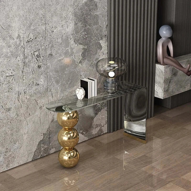 Modern interior with a gold side table, glass shelf, and decorative items against a marble wall.