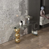 Modern interior with a gold side table, glass shelf, and decorative items against a marble wall.
