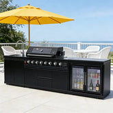 stainless steel outdoor kitchen on wheels with BBQ, fridge, sink, and grill cooktop in a scenic outdoor setting.