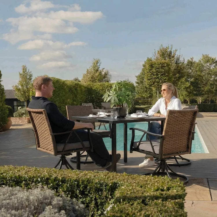 Two people sitting at a table outdoors with a pool and garden in the background