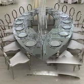 Large oval dining table with chairs and crystal chandelier in a formal setting.