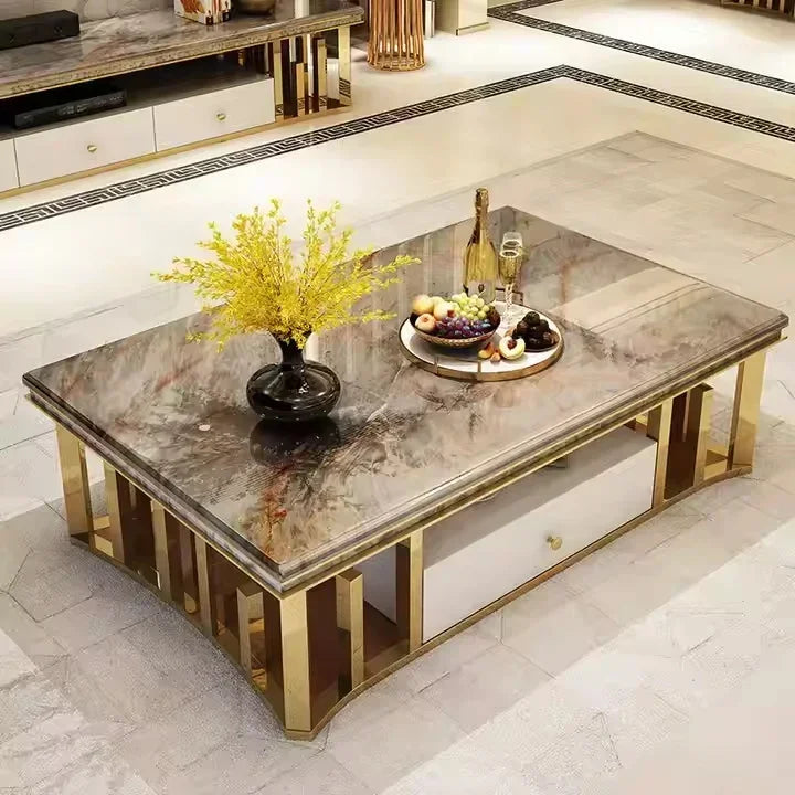 A modern rectangular coffee table with a polished gray and brown marble-patterned top and a gold-finished metal frame, shown in a luxury living room setting with decorative yellow flowers and fruit on top.