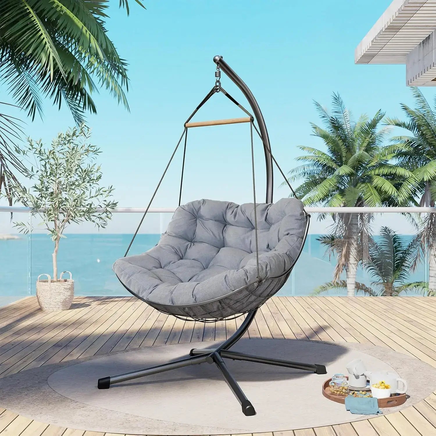 Hanging chair with gray cushion on a wooden deck with palm trees and ocean view