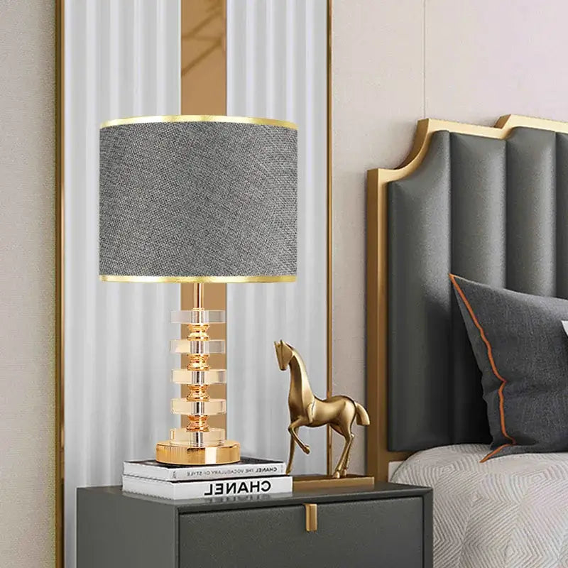 Modern crystal table lamp with fabric shade on a nightstand, featuring a gold finish and stylish design.